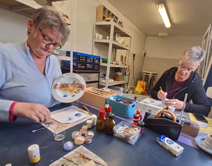 Regina Guggisberg und Mariette Guggisberg bemalen im Atelier Porzellan, vorne ein Kinderteller mit Blumen und Namensschriftzug